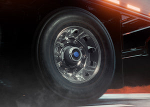 Close-up of a truck's wheel with visible tire and rim on a road at night.